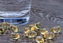 Carmenthin Kapseln liegen auf einem Holztisch neben einem Glas Wasser.