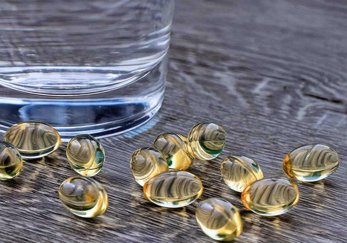 Carmenthin Kapseln liegen auf einem Holztisch neben einem Glas Wasser.