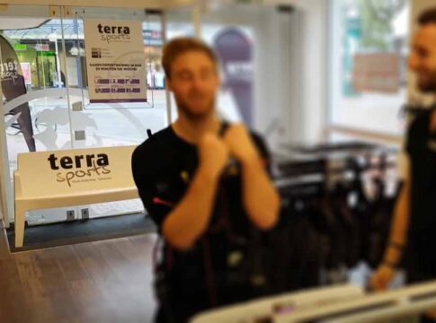 DeLaCruz vor dem EMS-Training im Terra Sports Studio Hamm, mit Trainer und sichtbarem Terra Sports Logo im Eingangsbereich.