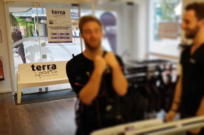 DeLaCruz vor dem EMS-Training im Terra Sports Studio Hamm, mit Trainer und sichtbarem Terra Sports Logo im Eingangsbereich.