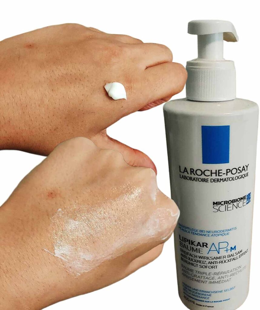 Auf dem Bild sieht man eine Hand, auf die der La Roche-Posay Lipikar Baume AP+M aufgetragen wird. Daneben steht die Flasche des Produkts. Die Creme ist reichhaltig und beruhigend. Sie ist ideal für trockene und empfindliche Haut.